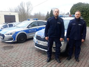 dwaj policjanci stoją przed radiowozem, z tyłu widoczne są inne policyjne auta