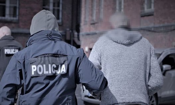 widziany od tyłu policjant prowadzący zatrzymanego mężczyznę