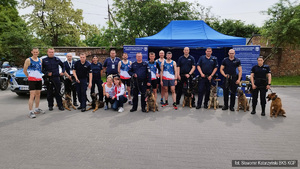 Grupa kilkunastu policjantów w tym: lekkoatleci, policjanci z psami. Wszyscy na tle stanowiska promocyjnego BKS KGP