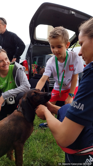 Policyjny pies z przewodnikiem. Kilkuletni chłopiec w biało - czerwonym stroju sportowym głaska policyjnego psa.