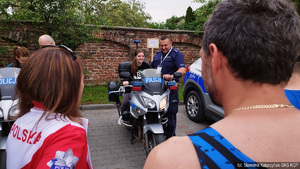 Uśmiechnięta niepełnosprawna uczestniczka biegu siedzi na policyjnym motocyklu, przy niej funkcjonariusz Policji w mundurze