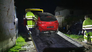 Zdjęcie przedstawia czerwony pojazd, który jest wciągany na lawetę. W tle widać dwie osoby ubrane w odblaskowe kombinezony