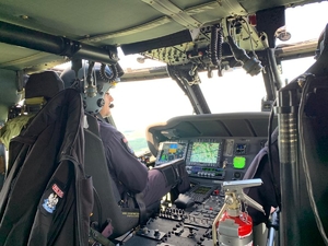 Wnętrze policyjnego Black Hawka podczas lotu, zdjęcie wykonane zza pleców pilotów, którzy siedzą za sterami maszyny. Na pierwszym z monitorów mapa, na sąsiednim - wskaźniki parametrów lotu.