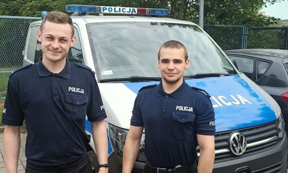 dwaj umundurowani policjanci stoją przy radiowozie