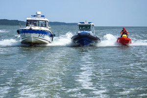 Dwie policyjne łodzie i strażak na skuterze wodnym płyną w szyku obok siebie.