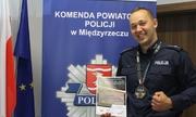 policjant prezentuje dyplom, na szyi ma medal, w tle baner z napisem Komenda Powiatowa Policji w Międzyrzeczu