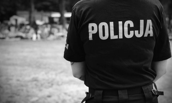 stojący tyłem policjant w koszulce z napisem Policja na plecach. Zdjęcie czarno - białe