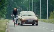 Kadr z filmu, mężczyzna jedzie na rowerze za nim samochód osobowy