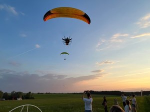 Na zdjęciu znajduje się asp. Grzegorz Bartosiewicz -dzielnicowy KP w Grabowie nad Pilicą na motoparalotni w powietrzu, na dole widać ludzi robiących mu zdjęcia