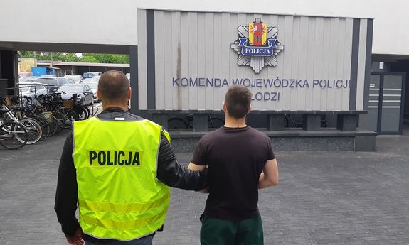policjant w kamizelce odblaskowej z napisem policja prowadzi na dziedzińcu komendy wojewódzkiej zatrzymanego oszusta