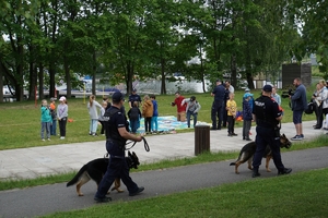 dwaj policjanci idą z psami służbowymi,  w tle dzieci z policjantami