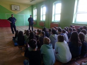 Policjanci w sali gimnastycznej rozmawiają z grupą dzieci.