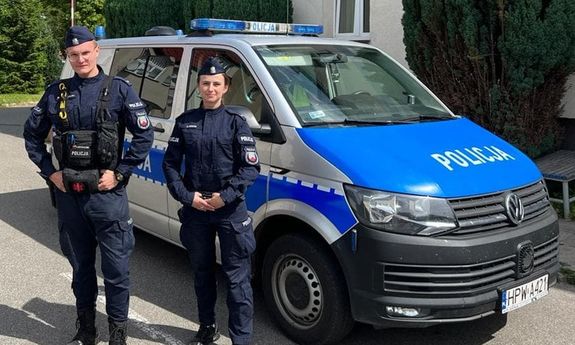 Umundurowani policjant i policjantka stoją przed radiowozem