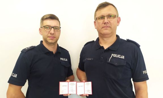 dwaj policjanci trzymają przed sobą legitymacje Złotej odznaki „ Zasłużony Dawca Krwi I Stopnia”