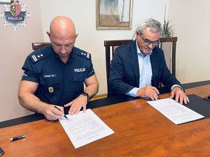 policjant z mężczyzną siedzą przy stole i podpisują dokumenty