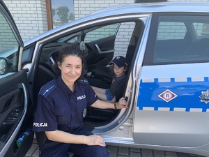 Policjantka pozuje do zdjęcia obok radiowozu w środku siedzi mały chłopiec.