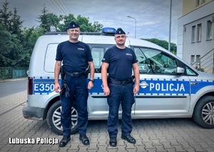 dwóch policjantów w mundurze stoi przy radiowozie