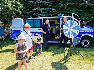 Policjanci stoją przy radiowozie i grają w grę plenerową z dziećmi.