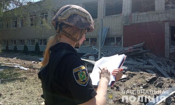 ukraińska policjantka dokumentująca zbrodnie wojenne stoi przed zbombardowanym budynkiem