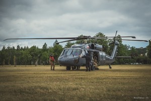 Policyjny Black Hawk stoi na trawiastym lądowisku przed dziobem maszyny dwoje crew chiefów podczas przygotowania maszyny do startu w bocznych drzwiach kilku kontrterorystów siedzących na pokładzie maszyny.