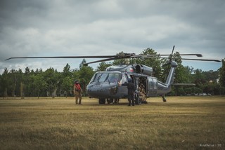 Policyjny Black Hawk stoi na trawiastym lądowisku przed dziobem maszyny dwoje crew chiefów podczas przygotowania maszyny do startu w bocznych drzwiach kilku kontrterorystów siedzących na pokładzie maszyny.