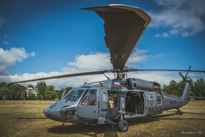 Zbliżenie na zaparkowany na trawiastym lądowisku policyjny śmigłowiec Black Hawk. W maszynie otwarte wszystkie drzwi.