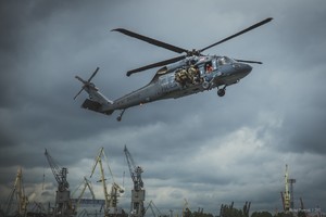 W tle portowych żurawi przelatuje policyjny Black Hawk, na którego prawej burcie trzech kontrterorystów szykujących się do desantu. W oknie śmigłowca crew chief w kamizelce ratunkowej.
