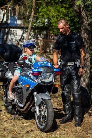 Dziecko w czapce policyjnej siedzi na motocyklu policyjnym obok stoi policjant.