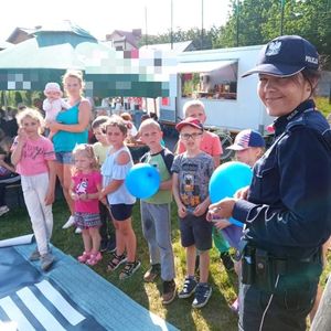Policjantka pozuje do zdjęcia z grupą dzieci, niektóre z nich trzymają w rękach balony.