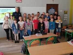 Policjantka w sali szkolnej pozuje do zdjęcia z grupą dzieci.