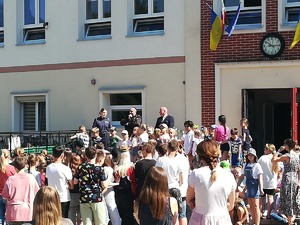 Policjantka z dużą grupą dzieci i ich opiekunami stoi przed wejściem do budynku szkoły.