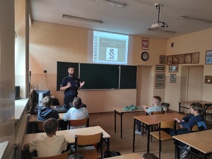 W sali szkolnej policjant rozmawia z grupą dzieci.