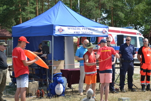 Pokaz ratowników wodnych po prawej stronie policjant i ratownicy medyczni w tle namiot profilaktyczny.