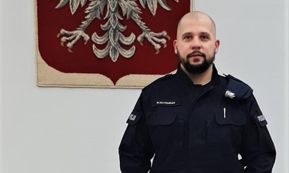 policjant w mundurze a za nim godło na ścianie