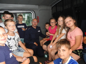 Policjant z grupą dzieci pozuje do zdjęcia w środku furgonetki policyjnej.