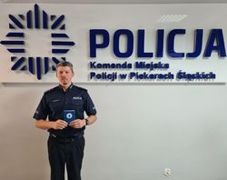 Umundurowany policjant trzyma w rękach legitymacje Wodnego Ochotniczego Pogotowia Ratunkowego. W tle napis &amp;amp;quot;Policja Komenda Miejska Policji w Piekarach Śląskich