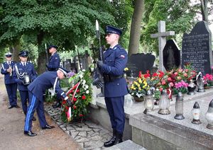 Komendant Główny Policji schyla się nad wieńcem złożonym przed grobem. Z boku, przy grobie dwaj policjanci pełnią wartę honorową
