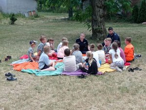 Policjanci na polanie siedzą z grupą  dzieci.