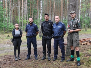 Policjanci, harcerze i strażak pozują w lesie do zdjęcia.