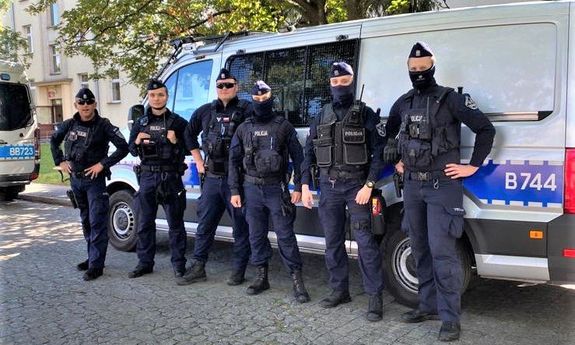 grupa policjantów stoi przed radiowozem