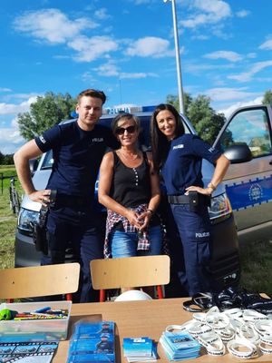 Policjanci pozują do zdjęcia na tle radiowozu, przed nimi stół z gadżetami i ulotkami promującymi akcję &quot;Kręci mnie bezpieczeństwo nad wodą&quot;.