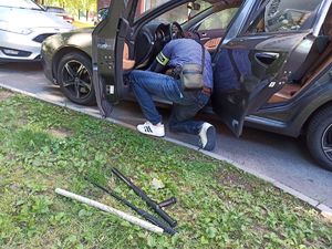 funkcjonariusz Straży Granicznej przeszukujący samochód, na trawie leżą niebezpieczne przedmioty ujawnione w samochodzie