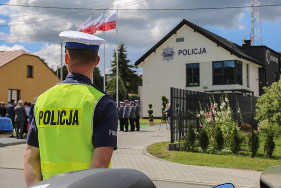 nowy budynek posterunku Policji, na pierwszym planie widoczny stojący tyłem policjant w żółtej kamizelce z napisem Policja na plecach