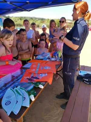policjantka rozmawia z dziećmi o bezpieczeństwie przekazując im materiały promujące akcję Kręci mnie bezpieczeństwo nad wodą