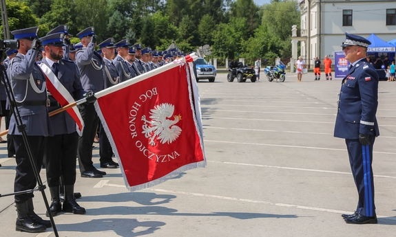 policjanci stoją w szeregu jeden z nich trzyma sztandar, naprzeciwko nich policjant salutuje