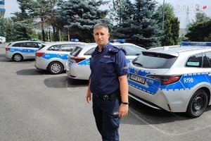 Zdjęcie kolorowe przedstawia policjanta na tle radiowozów policyjnych