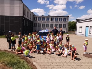Policjanci z grupą dzieci pozują do zdjęcia przy radiowozie.