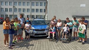 Policjantka z grupą dzieci pozuje do zdjęcia obok radiowozu.