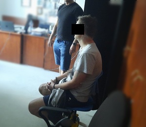 zatrzymany siedzi na krześle skuty w kajdanki, obok stoi nieumundurowany policjant