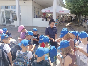 Policjantka rozdaje grupie dzieci ulotki akcji &quot;Kręci mnie bezpieczeństwo nad wodą&quot;.